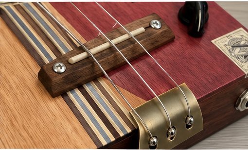 Close-up of the guitar's wooden bridge, bone saddle and brass tailpiece where the three strings anchor