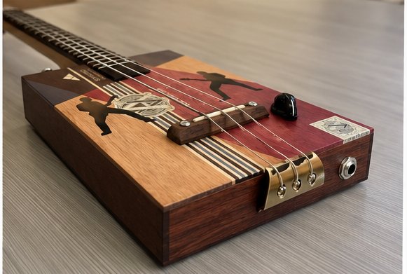 Low-angle view of the finished cigar box guitar, showing the full length of the neck and fretboard leading down to the cigar-box body