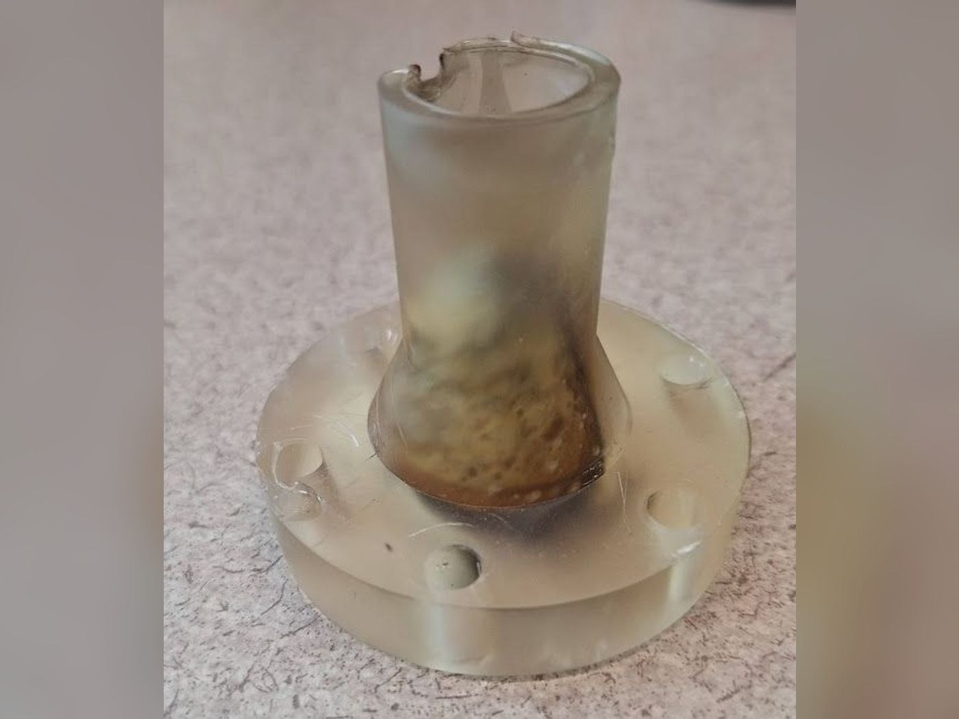 The 3D-printed translucent resin nozzle standing on a table after its hot-fire test, with a scorched, discolored bore and a chipped exit rim