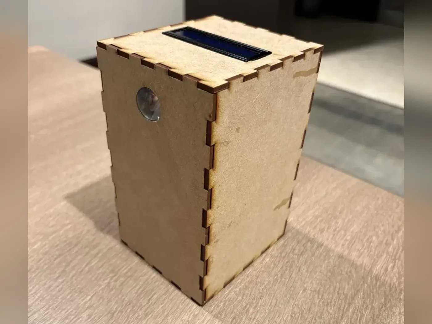The receiver, a tall laser-cut box with an LCD set into the lid and a round lens window on the front