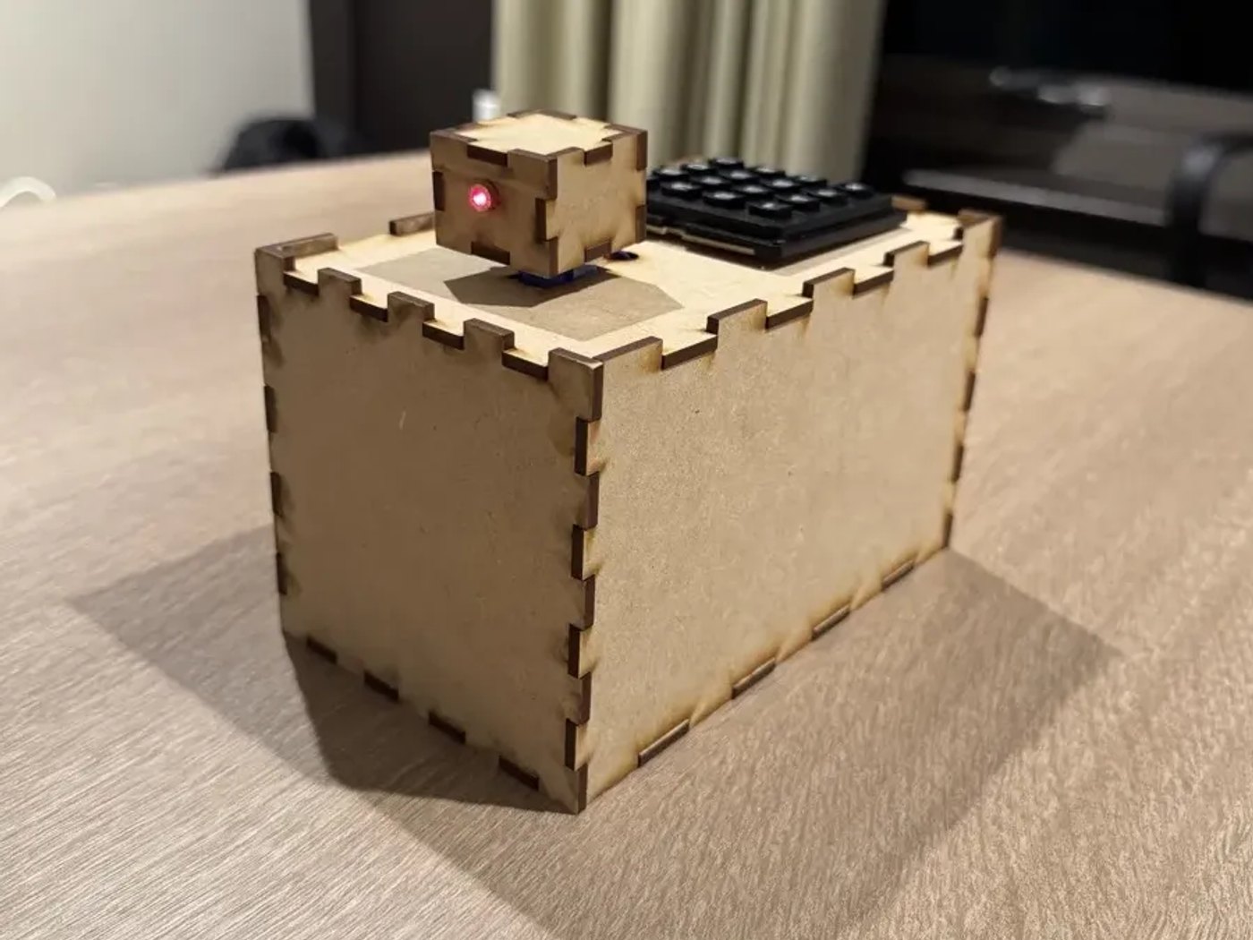 The finished transmitter, a laser-cut box with a 16-key keypad and a small servo-mounted laser housing on its lid, with the red laser dot lit