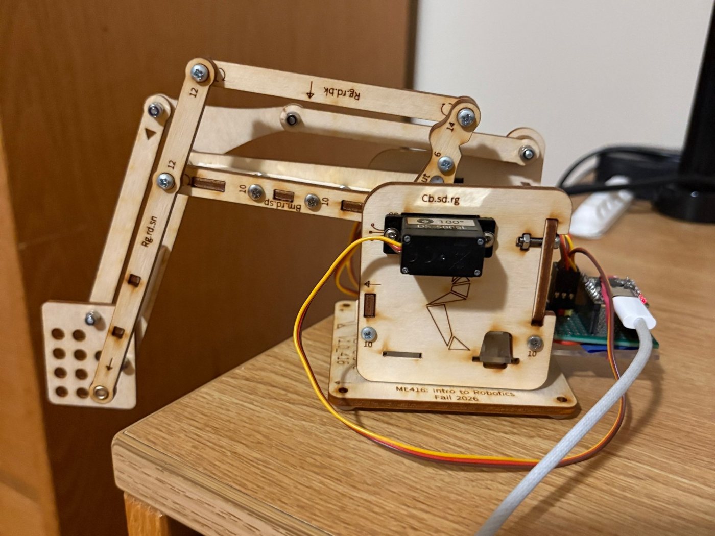 Three-quarter view of the robotic arm reaching out to the left and down from its base, with the end plate close to the table